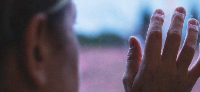 A woman peers out from behind a glass window, appears trapped