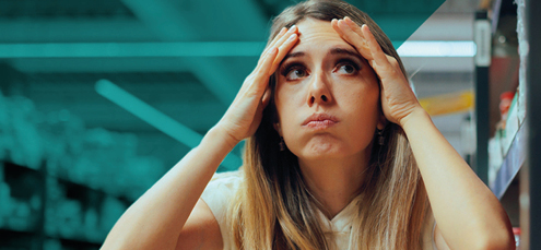 Woman in supermarket raises hands to her head in confusion and worry over which products might cause cancer