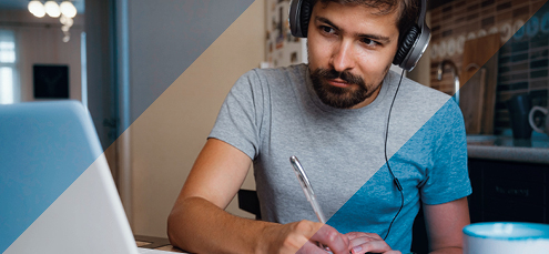 bearded man takes notes listening to a webinar on a laptop with earphones