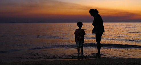 mother and son in silhouette standing in the sea at sunset