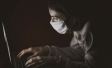 Image of woman wearing mask typing on laptop