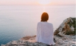 Woman sitting alone with back toward camera looking out at water