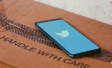 Phone screen showing twitter logo placed on cardboard box labeled as "Handle with care"