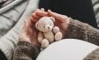 Woman pregnant belly with little teddy toy bear.