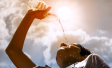 Young woman drinking fresh water from a plastic bottle under the hot summer sun