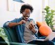 man sat on sofa looking happy whilst scrolling on his phone