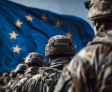 Uniformierte Soldaten stehen mit dem Rücken zur Kamera vor der wehenden EU-Flagge