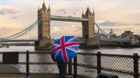 A tourist with a British (Union Jack) flag umbrella watching the sunset over Tower Bridge, London