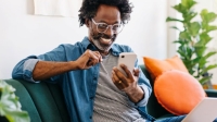 man sat on sofa looking happy whilst scrolling on his phone
