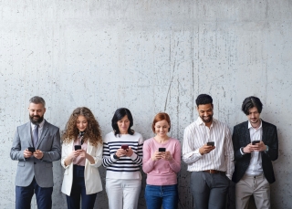Sechs Personen stehen vor einer Wand und schauen auf ihr Smartphones
