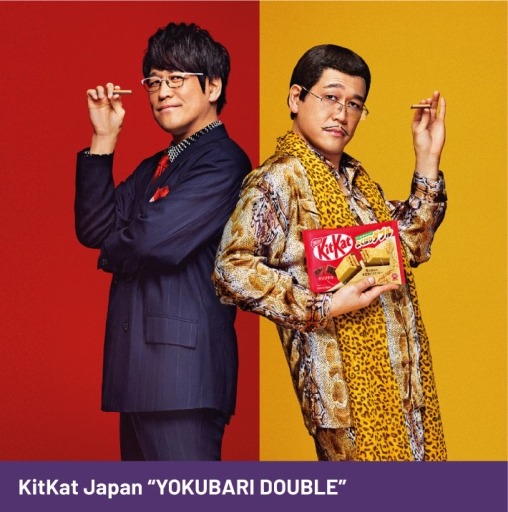Japanese comedian, Daimaou Kosaka standing back-to-back with his alter-ego Pikotaro while both hold the KitKat Yokubari Double.