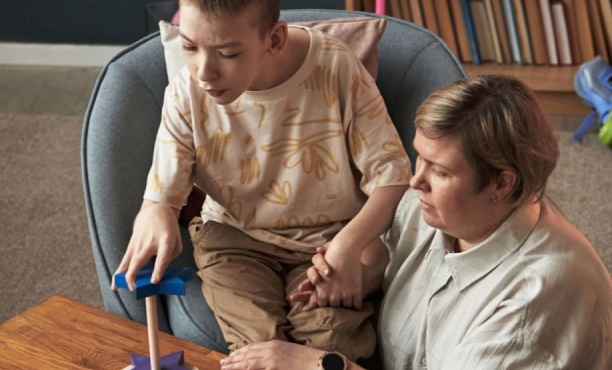 young boy with disability sat playing with his carer