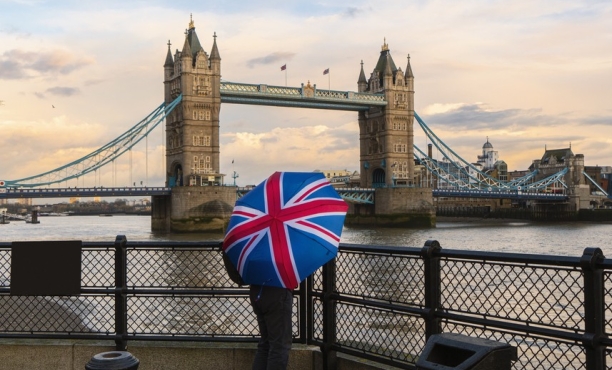A tourist with a British (Union Jack) flag umbrella watching the sunset over Tower Bridge, London