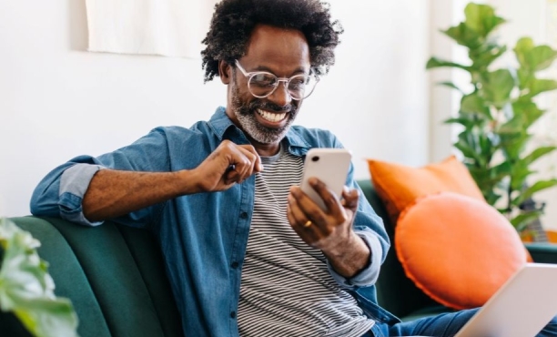 man sat on sofa looking happy whilst scrolling on his phone