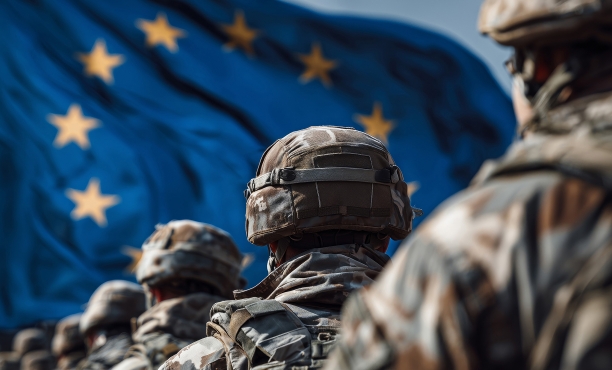Uniformierte Soldaten stehen mit dem Rücken zur Kamera vor der wehenden EU-Flagge