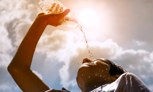 Young woman drinking fresh water from a plastic bottle under the hot summer sun