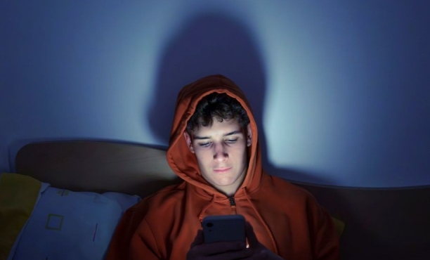 young man sat in the dark illuminated by his smart phone screen