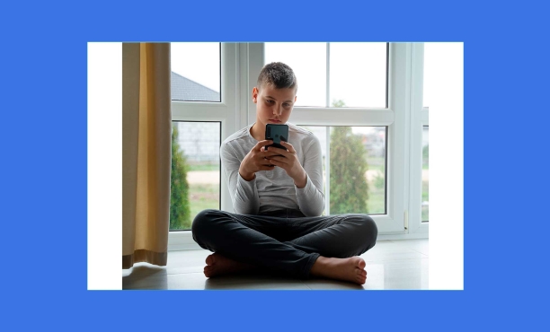 Jovem mexendo no celular sentado no chão de casa