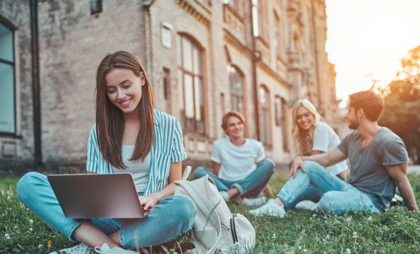A group of young people sit on the grass with a laptop