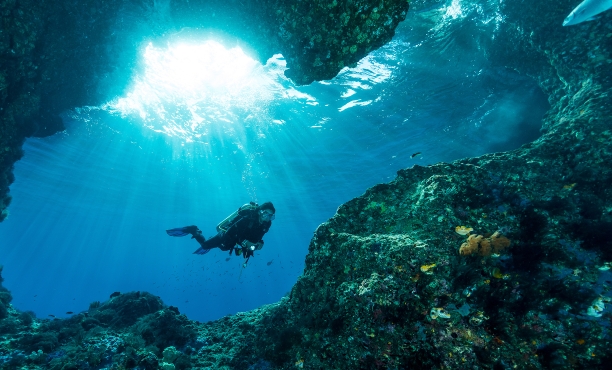 Taucherin unter Wasser am Eingang einer Höhle, durch die Sonnenstrahlen scheinen | Ipsos