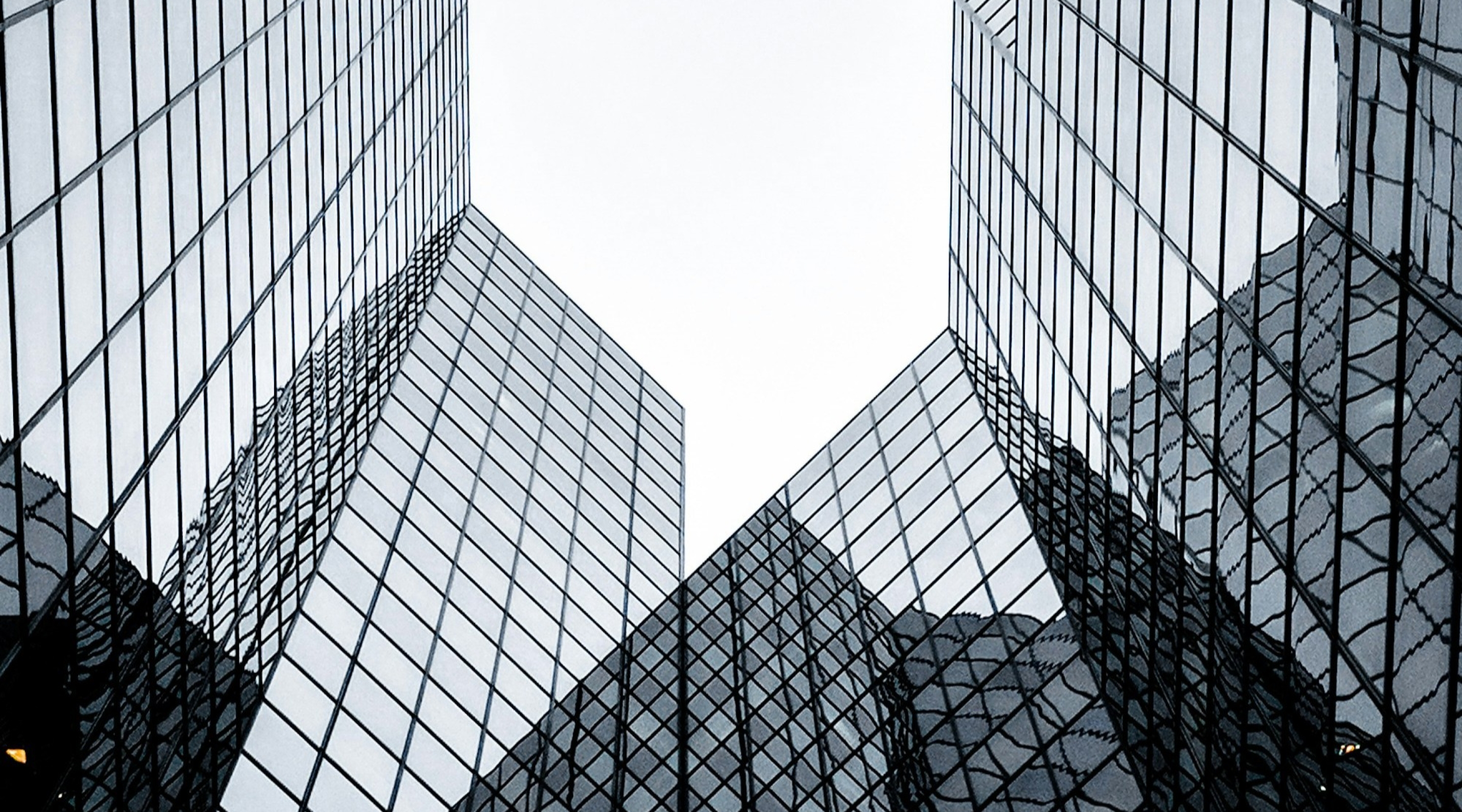 A dramatic upward view of modern glass buildings with metal architectural structures curving overhead.