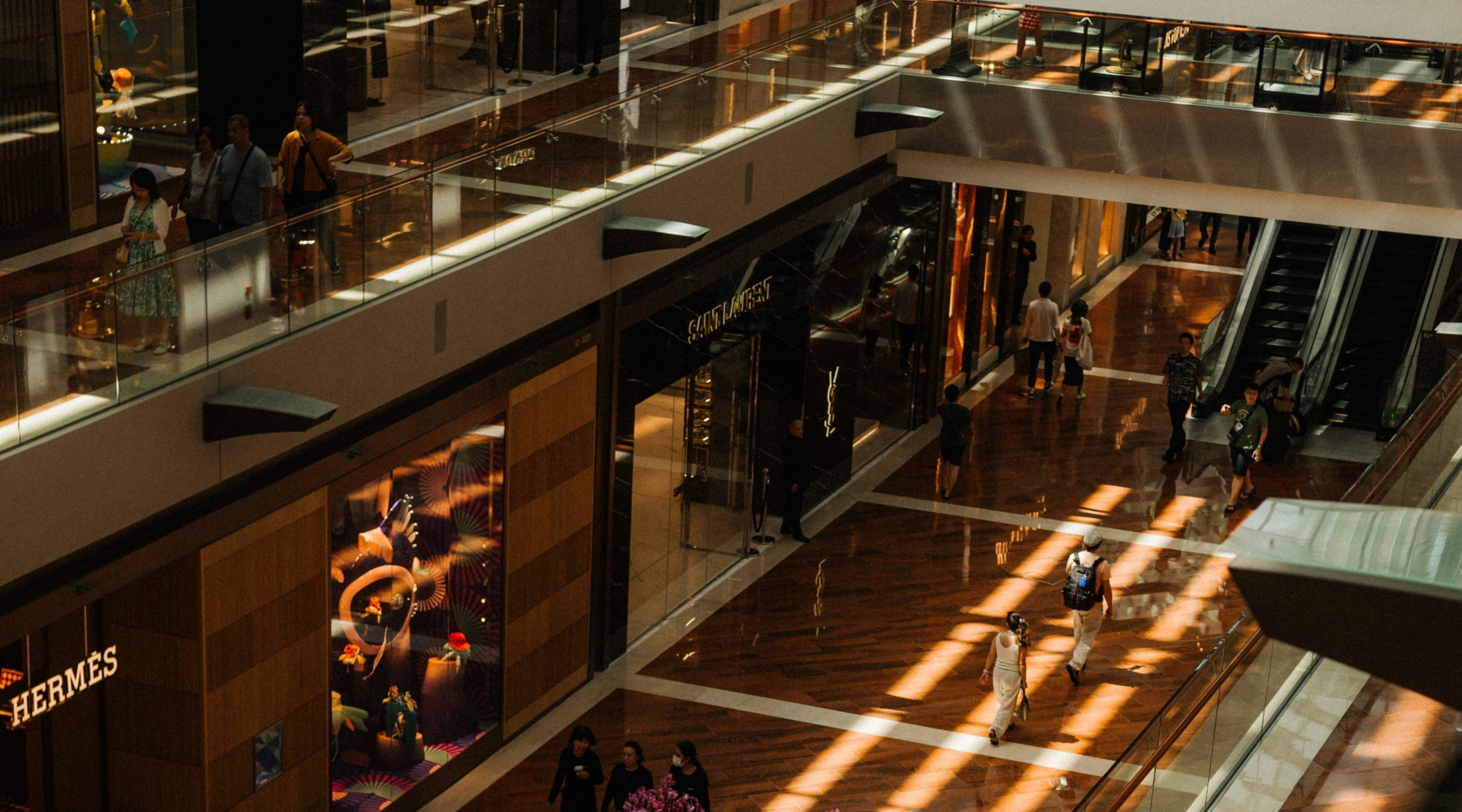 Shoppers walking through a modern outdoor shopping arcade with glass storefronts.