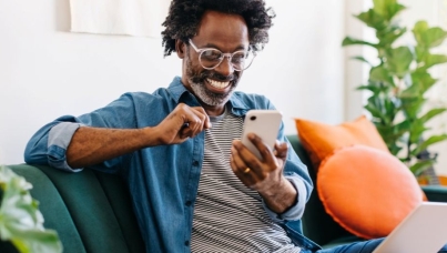 man sat on sofa looking happy whilst scrolling on his phone