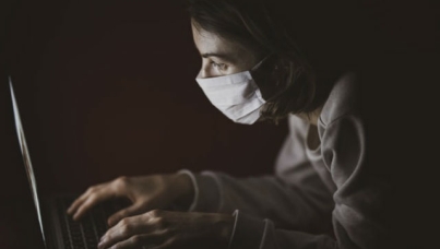 Image of woman wearing mask typing on laptop