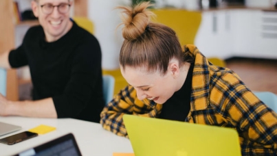 Image of woman and man laughing while working behind laptop