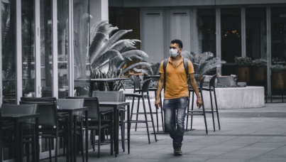 Man wearing mask walks by empty chairs outside restaurant