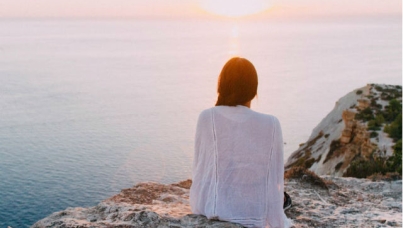 Woman sitting alone with back toward camera looking out at water