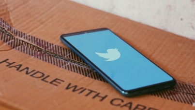 Phone screen showing twitter logo placed on cardboard box labeled as "Handle with care"