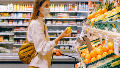 Woman wearing mask in grocery store and selecting produce. She is holding a lemon