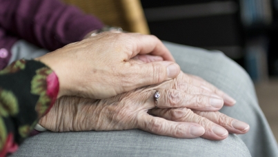 One old person's hand holding another old person' hand with ring on the ring finger