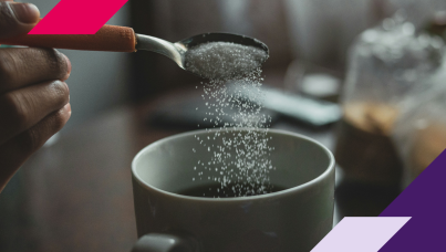 Picture of a hand pouring sweetener into a cup of coffee