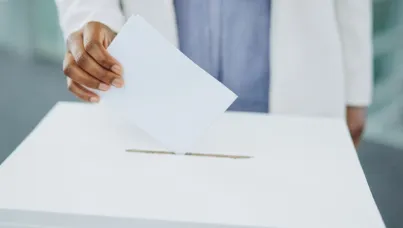 A hand casting a ballot into a box