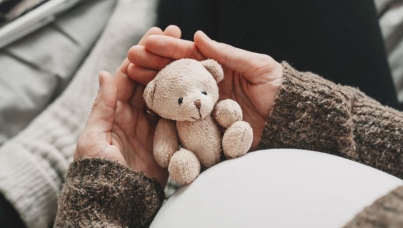 Woman pregnant belly with little teddy toy bear.