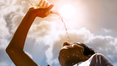 Young woman drinking fresh water from a plastic bottle under the hot summer sun