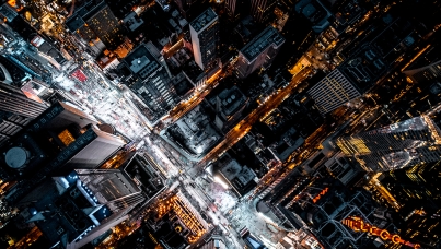 A nighttime aerial view of a brightly lit city intersection with surrounding skyscrapers
