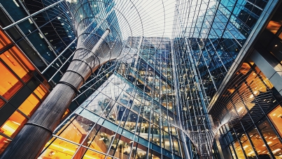 A dramatic upward view of modern glass buildings with metal architectural structures curving overhead.