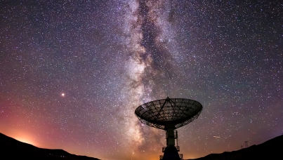 A radio telescope silhouetted against the star-filled Milky Way at night.