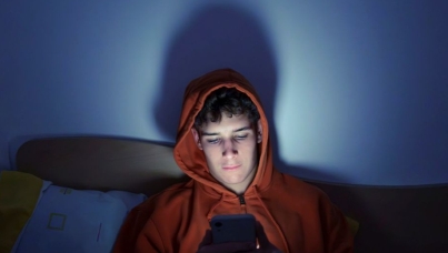 young man sat in the dark illuminated by his smart phone screen