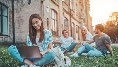 A group of young people sit on the grass with a laptop