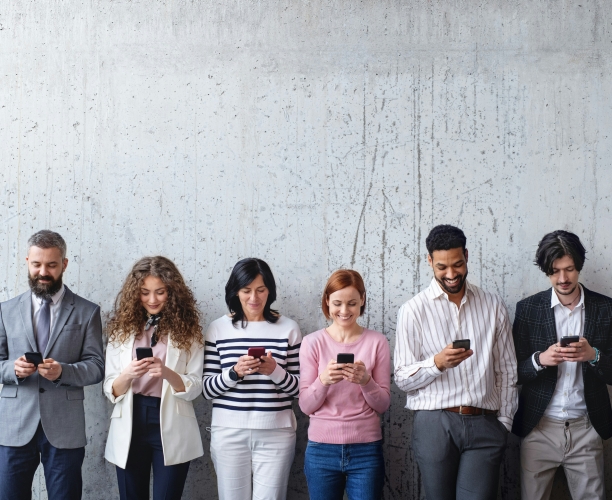 Sechs Personen stehen vor einer grauen Wand und schauen auf ihr Smartphone