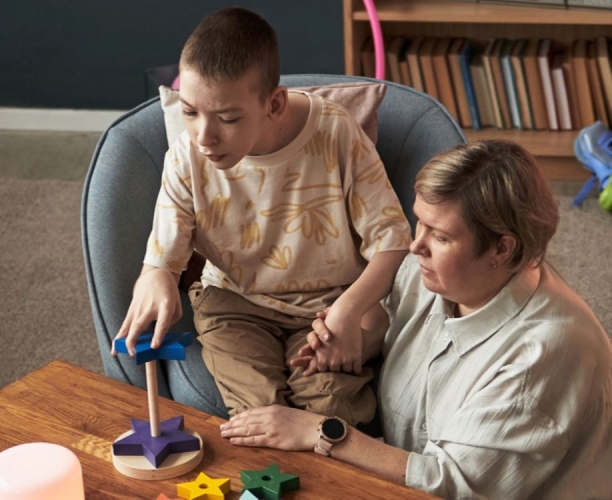young boy with disability sat playing with his carer