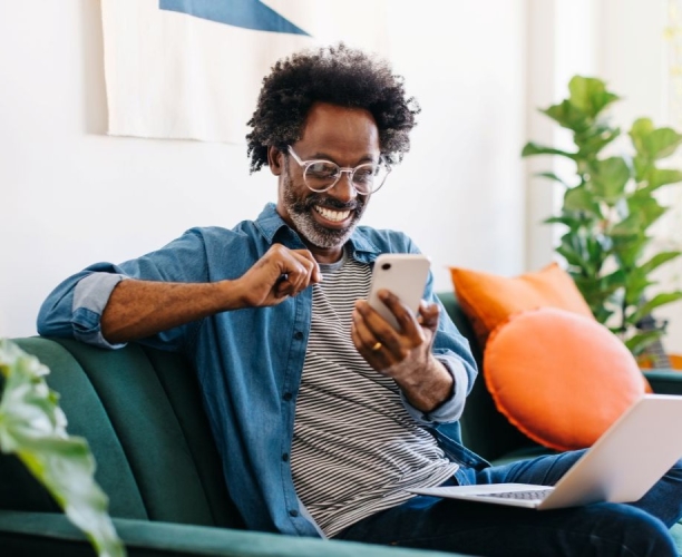man sat on sofa looking happy whilst scrolling on his phone