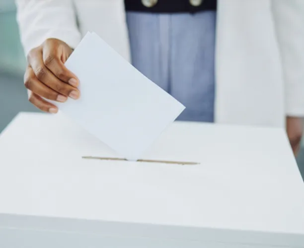 A hand casting a ballot into a box