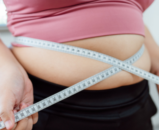An overweight woman measuring her stomach with a tape