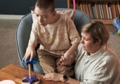 young boy with disability sat playing with his carer